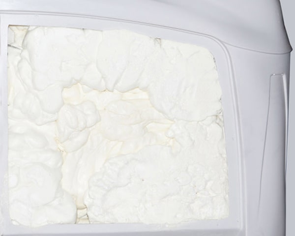 Rectangular block of white dairy product (likely cream cheese) inside a white plastic tub.