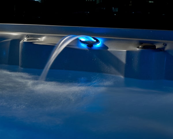 Blue LED light in a hot tub or spa jet area with water flowing from a spout into foamy water at night (informative detail)