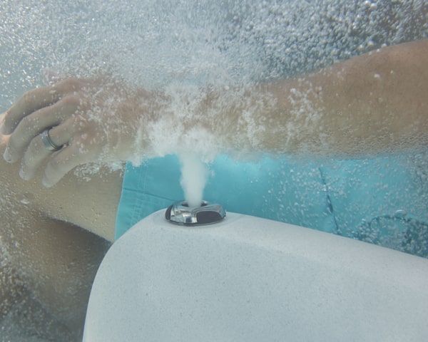 Close-up of a hand with a ring pressing the toilet flush button on the tank, with bubbles spraying around.
