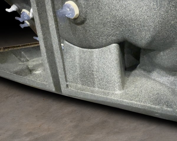 Close-up of a gray metal machine base with a small blue knob and beige cap, on a concrete workshop floor.
